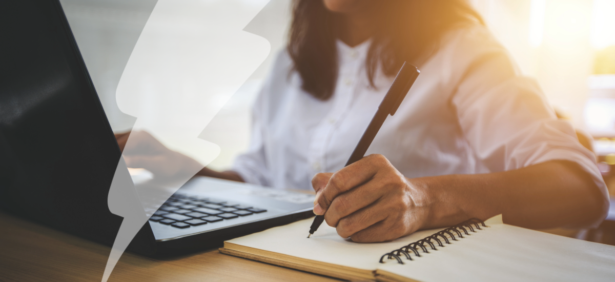 A woman sat by a desk and laptop, learning during online courses using a notebook.