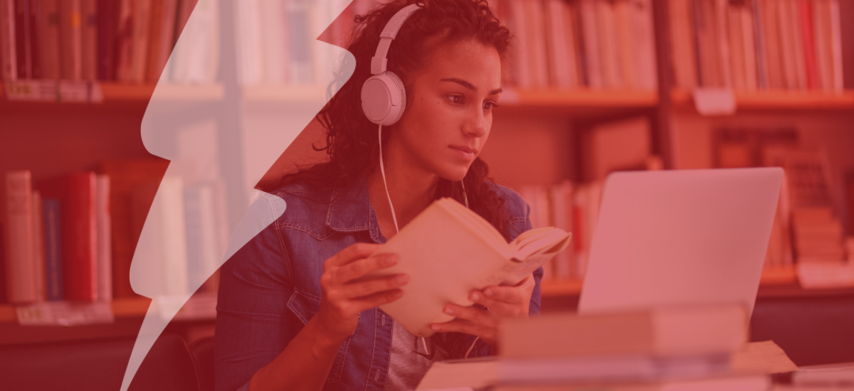 Young female student studying in a university library. She is using a laptop and learning online.